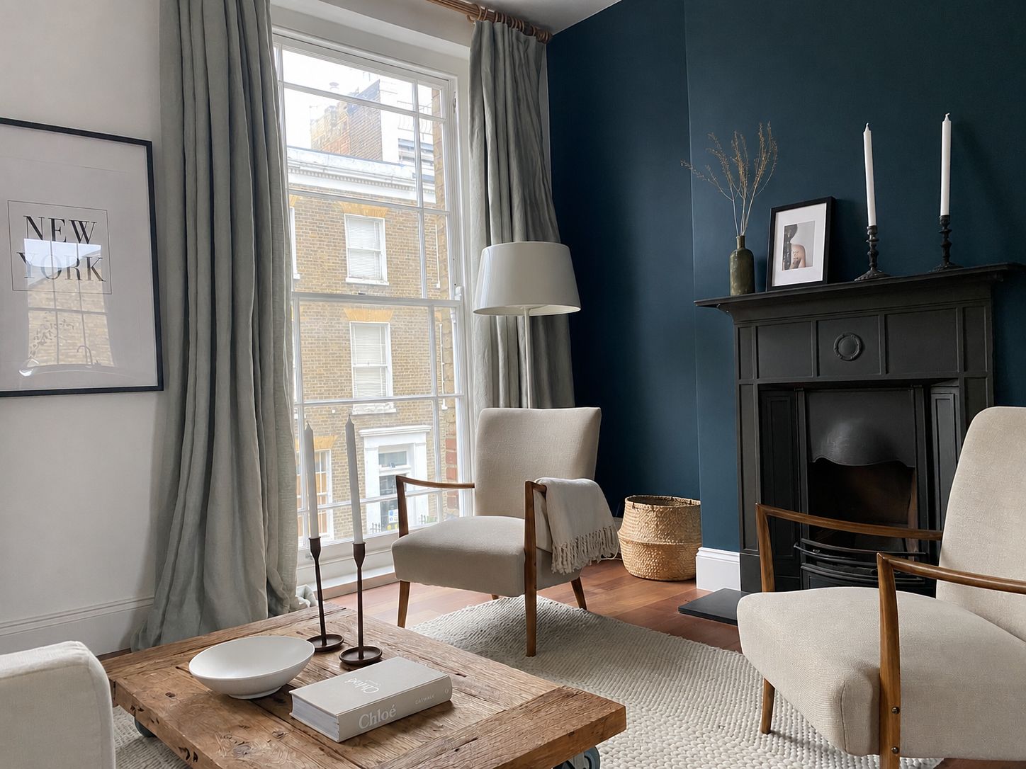 Deep teal sitting room with grey curtains, vintage fireplace and rattan chair